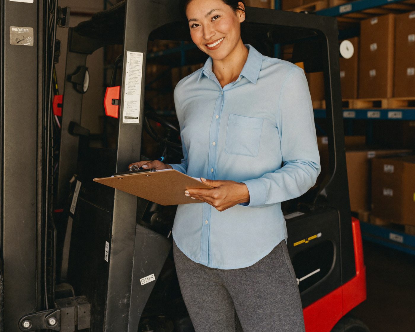 A warehouse owner with a clipboard standing beside her forklift
